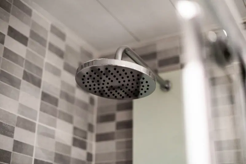Rain shower head with water streaming down past gray wall tiles